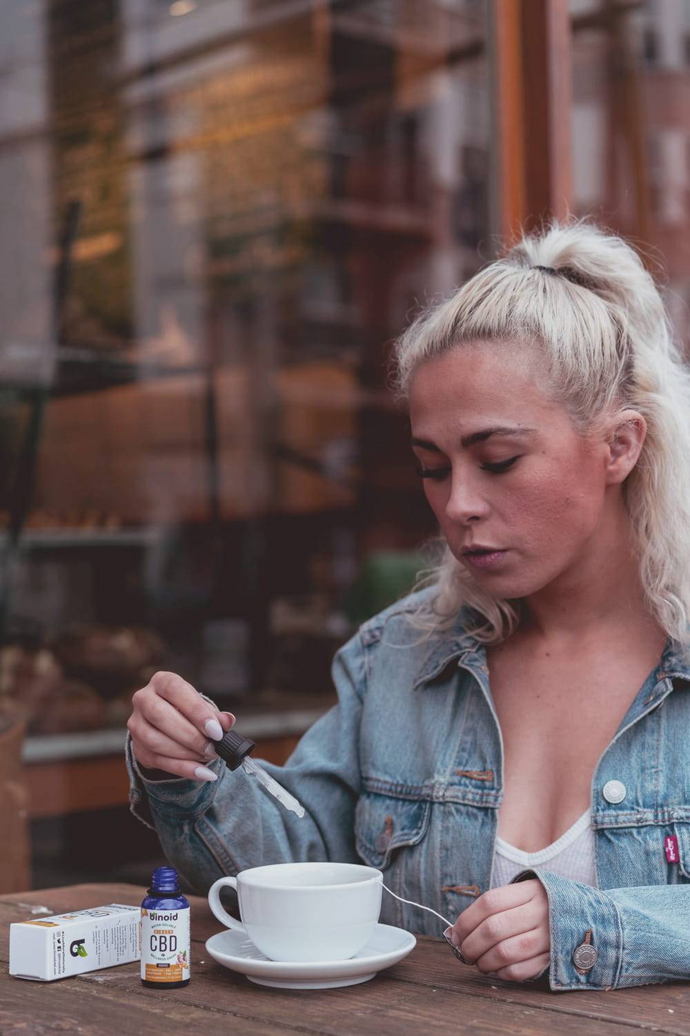 Eine Frau am Tisch nutzt eine Pipette, um CBD Öl in ein Getränk zu geben