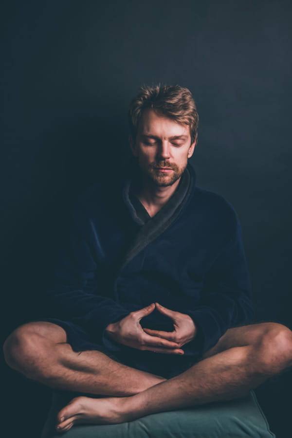 Sitzender Mann mit geschlossenen Augen in meditativer Haltung vor dunklem Hintergrund