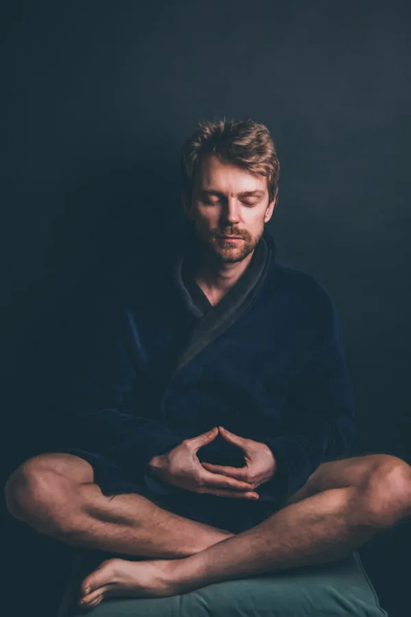 Meditativer Mann in dunkler Atmosphäre Sitzender Mann mit geschlossenen Augen in meditativer Haltung vor dunklem Hintergrund
