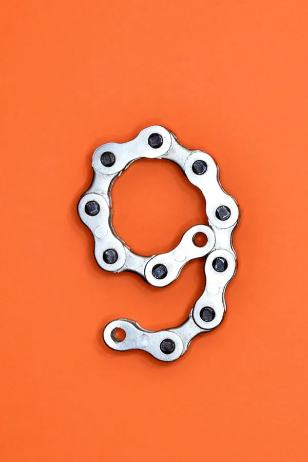 Zahl 9 aus Fahrradkette auf orangefarbenem Hintergrund Kreativ gelegte Zahl 9 aus einer Fahrradkette auf orangefarbenem Hintergrund