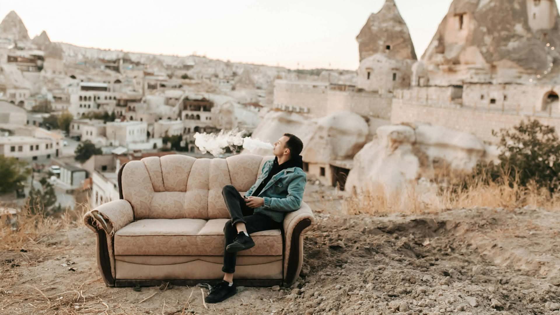 4MY Markenwelt: Lifestyle und eigenständiger Markenauftritt Mann sitzt auf einem Sofa im Freien vor einer felsigen Landschaft und stößt eine weiße Dampfwolke aus