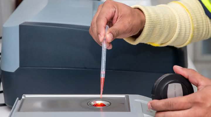 Eine Person führt mit einer Pipette eine Flüssigkeit in ein Laborgerät zur Analyse ein