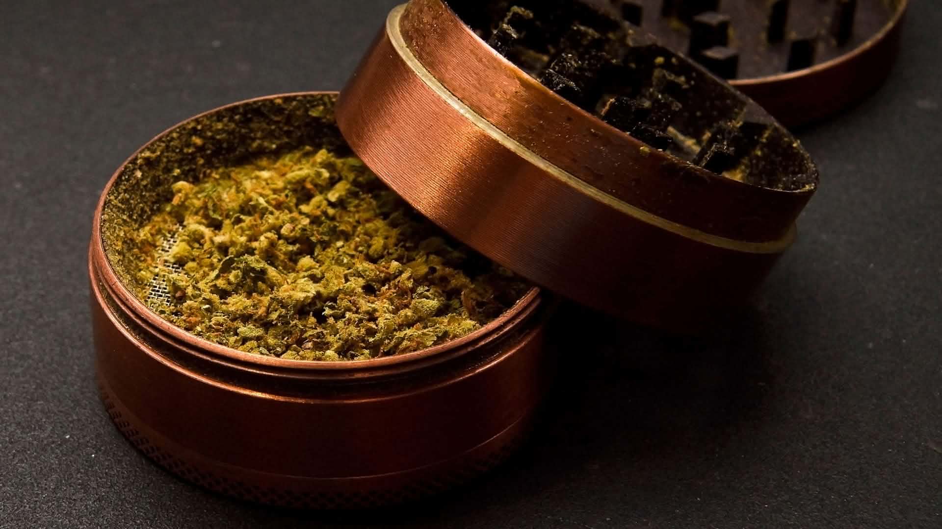 Superior Blend und Cannabinoid-Mischungen Geöffneter kupferfarbener Grinder mit zerkleinertem Cannabis auf dunklem Untergrund.